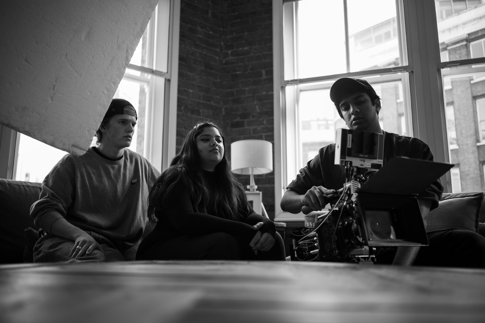 Three crew watching a take on the monitor beside a cinema camera, backlit by tall studio windows.