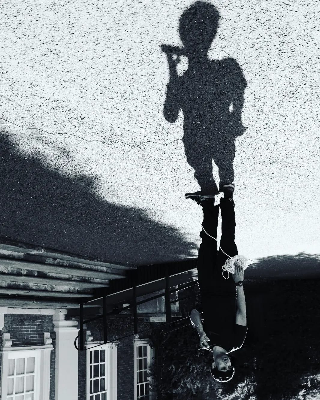 A black-and-white reflection of a crew member walking while coiling cable, shot upside down in a puddle.